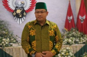 Seorang pria mengenakan pakaian batik hijau dan peci hijau sedang berdiri dalam acara resmi HIPNUSA sambil menyampaikan pesan organisasi.